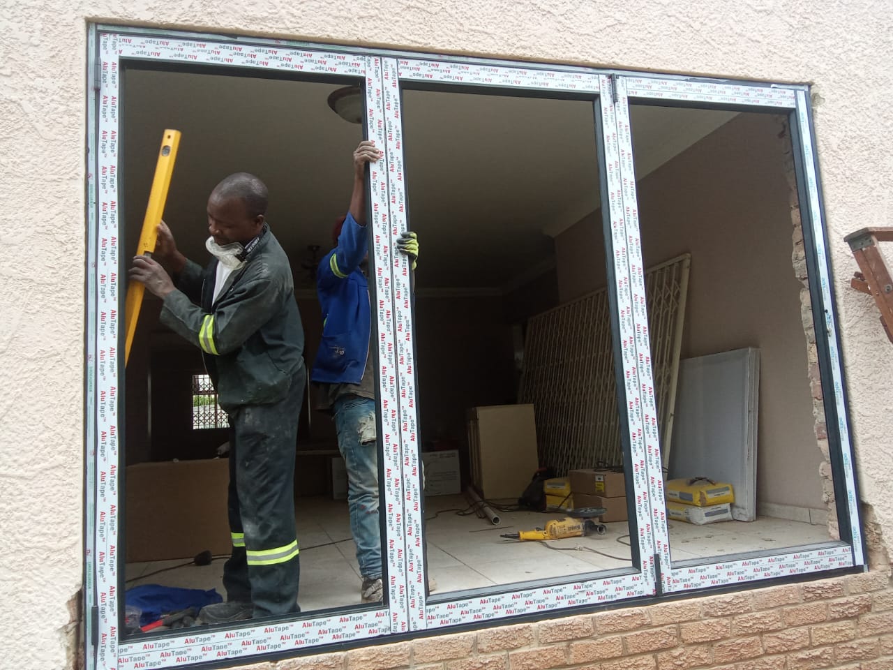 Workers levelling an aluminium window frame during installation in a plastered wall