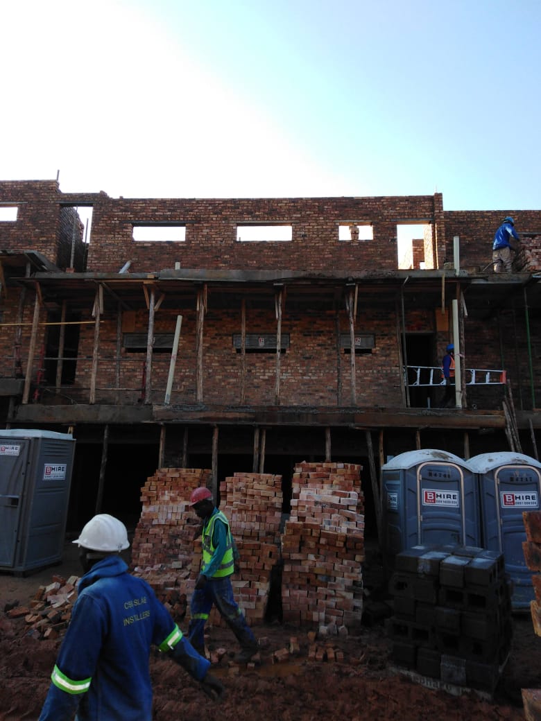 Multi-storey face-brick complex units under construction with scaffolding and brick stacks on site