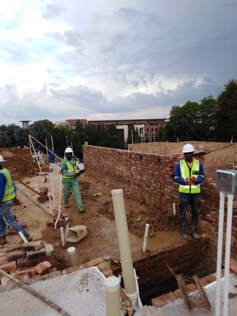 Bricklayers building walls between complex units with scaffolding and pipework installed