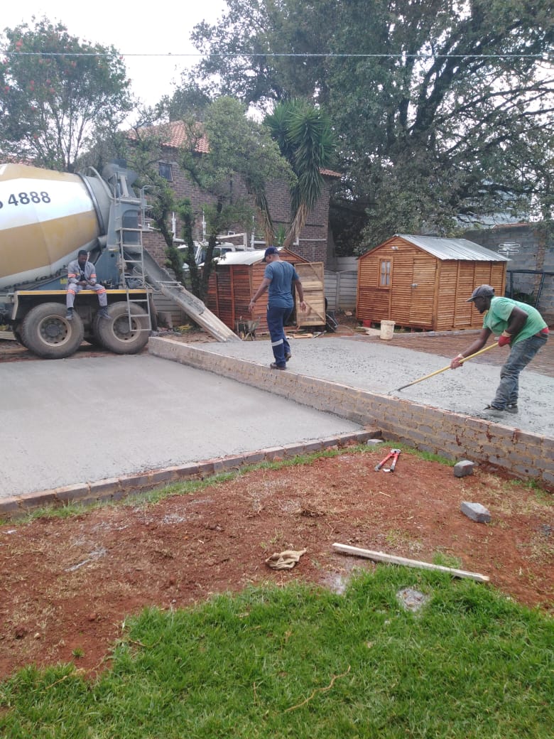 Workers screeding a new concrete slab edged with brick kerbing on a residential site