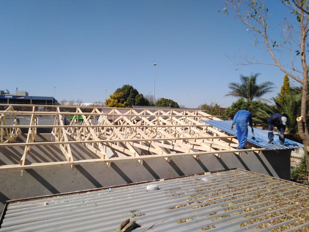 Workers fitting corrugated roof sheeting onto a new timber truss roof